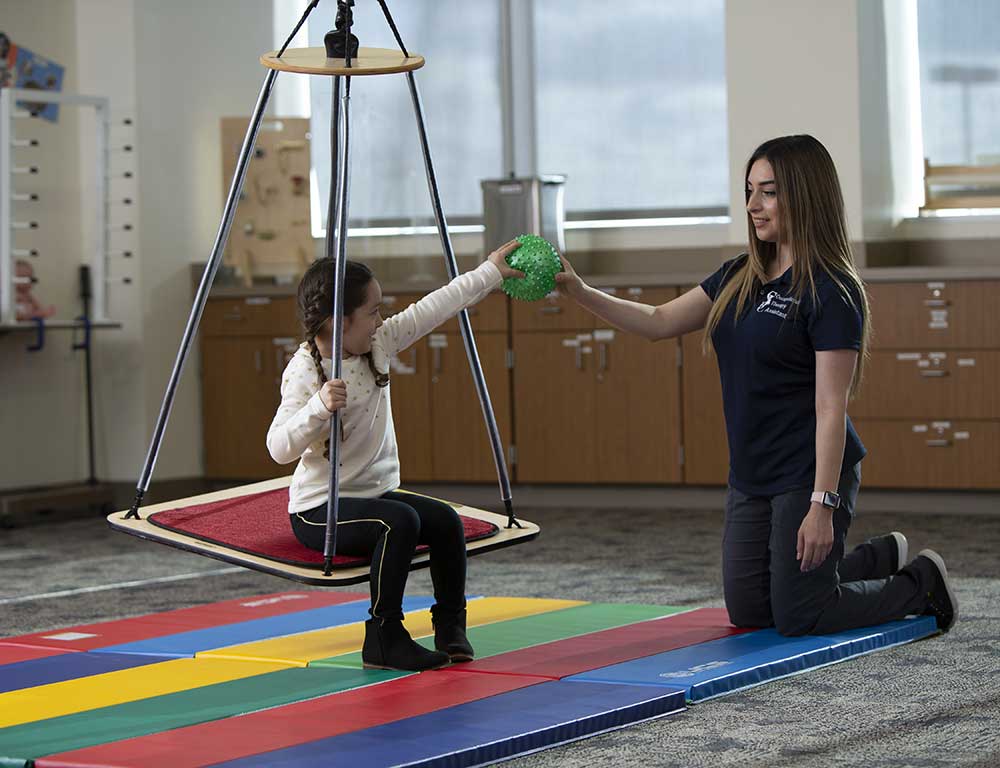 Occupational Therapy Assistant hands a ball to a child patient